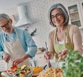 Older man and woman smiling and cooking a healthy meal at home