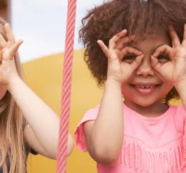 Two smiling young girls acting like they are wearing glasses by using their hands