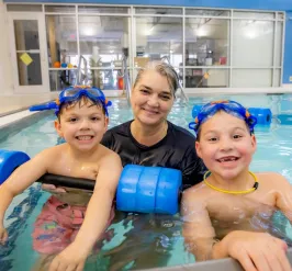 Swim instructor in pool with two smiling young boys