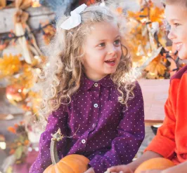 Kids holding pumpkins sitting outside in the fall