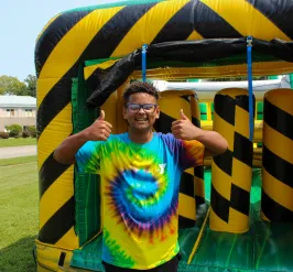 Boy with tie dye YMCA shirt smiling next to bouncy house