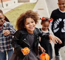 Four kids wearing Halloween costumes walking down a street