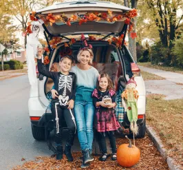 A woman and two kids sitting on the back of a car that has Halloween decorations